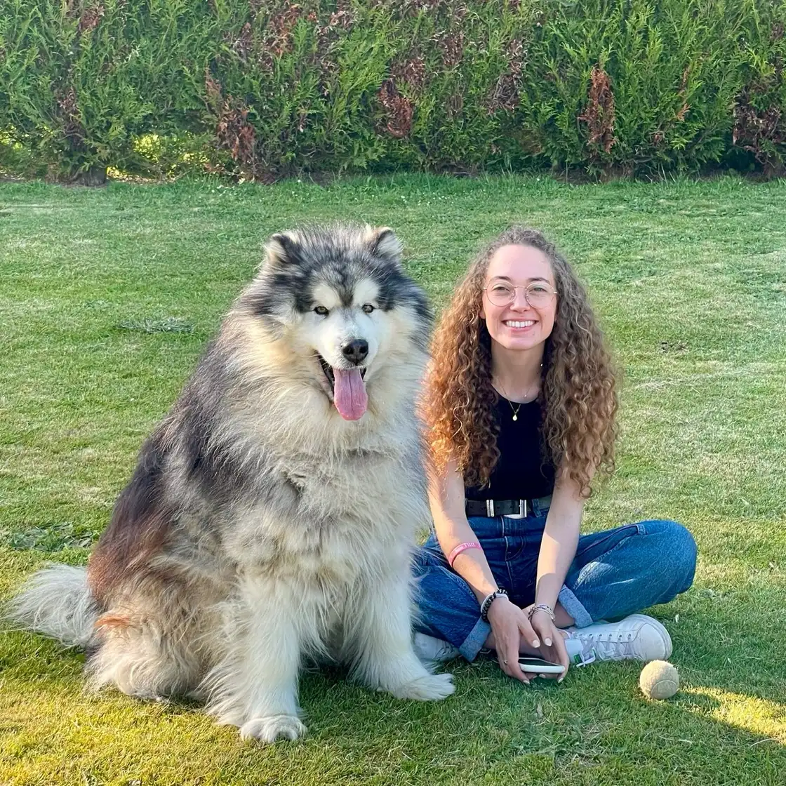 Maya assise dans l’herbe à côté d’un grand chien